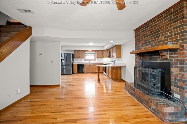 living room featuring ceiling fan, sink, a textured ceiling, light hardwood / wood-style flooring, and a fireplace