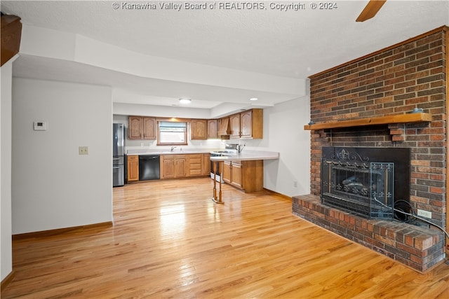 kitchen with a brick fireplace, light wood-type flooring, a textured ceiling, and appliances with stainless steel finishes