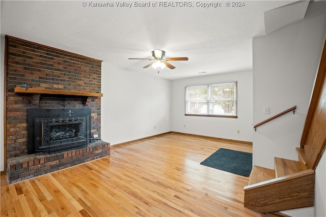 unfurnished living room featuring a textured ceiling, ceiling fan, a brick fireplace, and hardwood / wood-style flooring