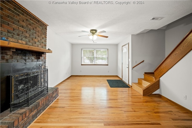 unfurnished living room featuring light wood-type flooring, a textured ceiling, ceiling fan, and a brick fireplace