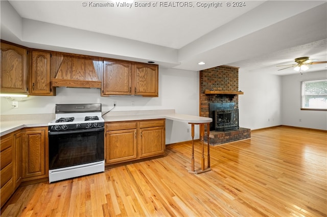 kitchen featuring custom range hood, a fireplace, light hardwood / wood-style flooring, white range with gas cooktop, and ceiling fan