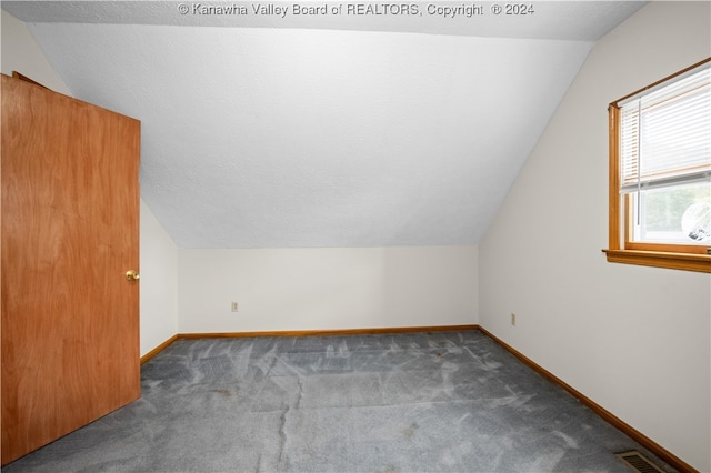 bonus room with a textured ceiling, lofted ceiling, and dark colored carpet