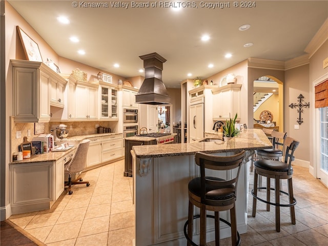 kitchen with custom exhaust hood, decorative backsplash, a large island with sink, ornamental molding, and paneled built in refrigerator