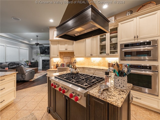 kitchen with appliances with stainless steel finishes, premium range hood, cream cabinets, and light tile patterned floors