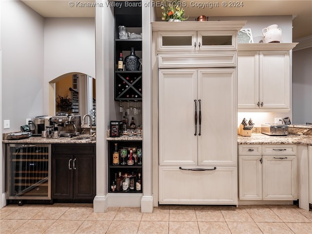 bar featuring wine cooler, light stone countertops, light tile patterned floors, and paneled fridge