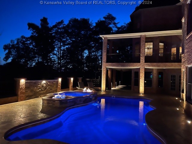 pool at twilight featuring an in ground hot tub and a patio