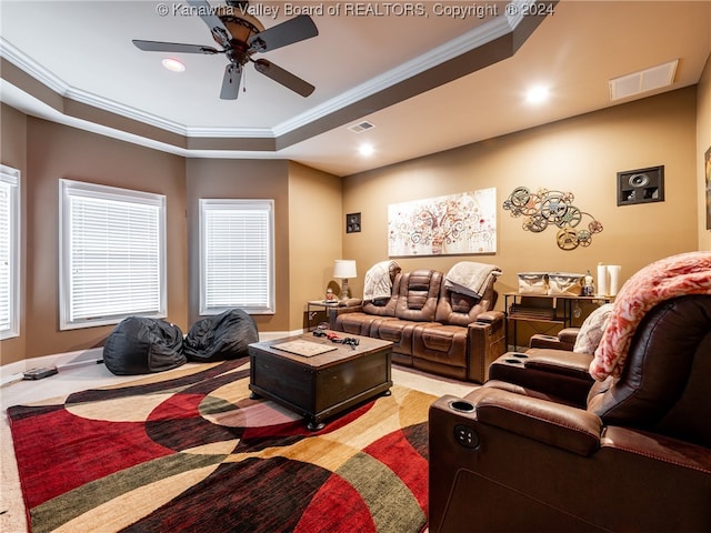 carpeted home theater with ornamental molding, a tray ceiling, and ceiling fan