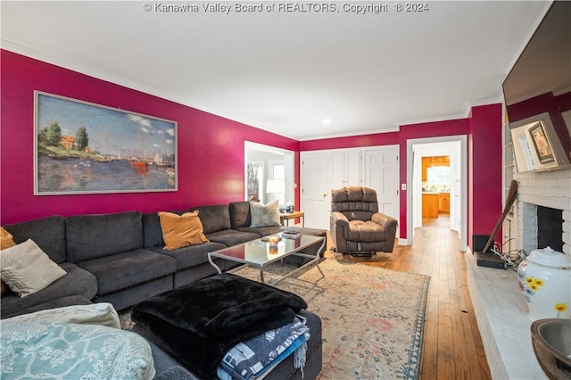 living room featuring wood-type flooring, a brick fireplace, plenty of natural light, and crown molding