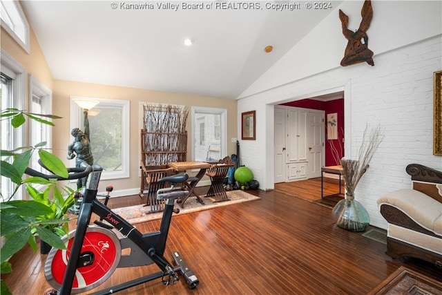 exercise area featuring brick wall, wood-type flooring, and vaulted ceiling