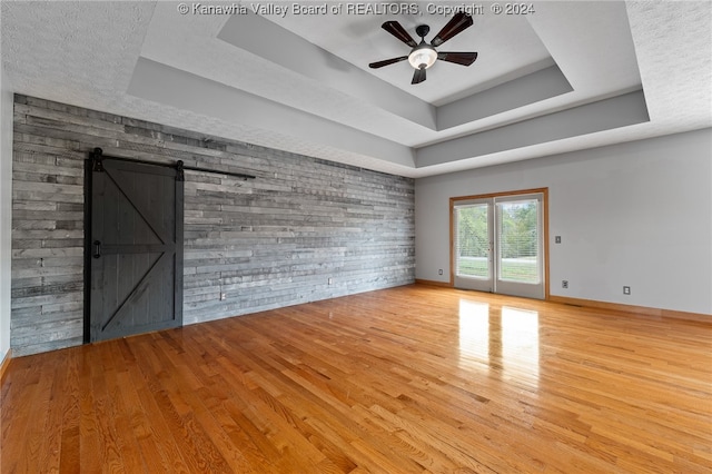 interior space with wood walls, ceiling fan, a raised ceiling, and a barn door