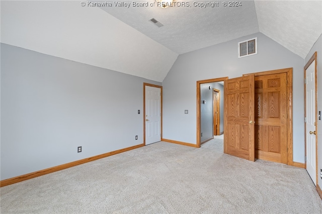 unfurnished bedroom with lofted ceiling, a textured ceiling, and light colored carpet