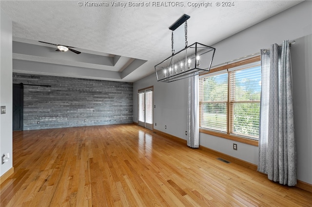 interior space featuring ceiling fan with notable chandelier, wood-type flooring, a healthy amount of sunlight, and a barn door