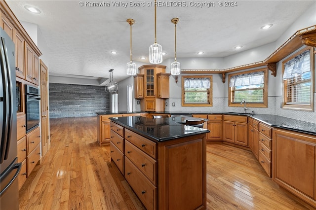 kitchen with pendant lighting, a kitchen island, a textured ceiling, stainless steel appliances, and light wood-type flooring