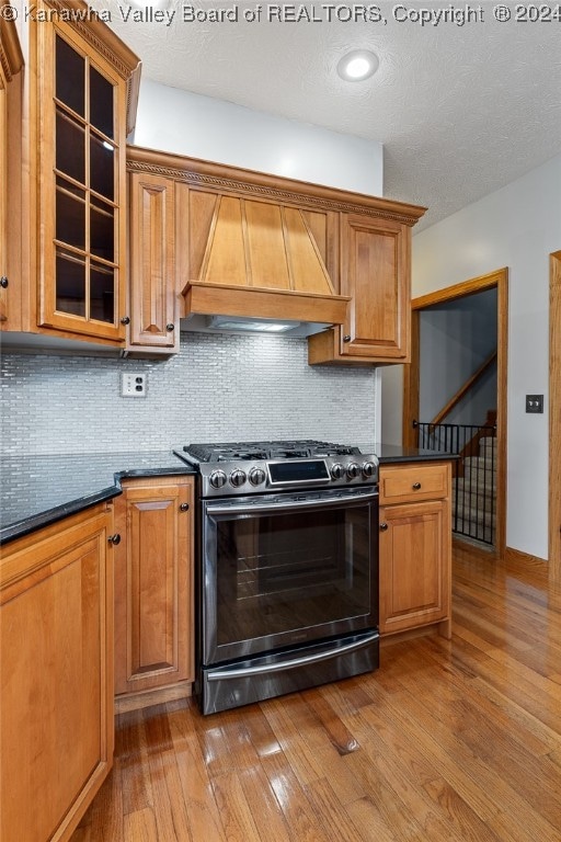 kitchen featuring gas stove, backsplash, custom range hood, and light wood-type flooring