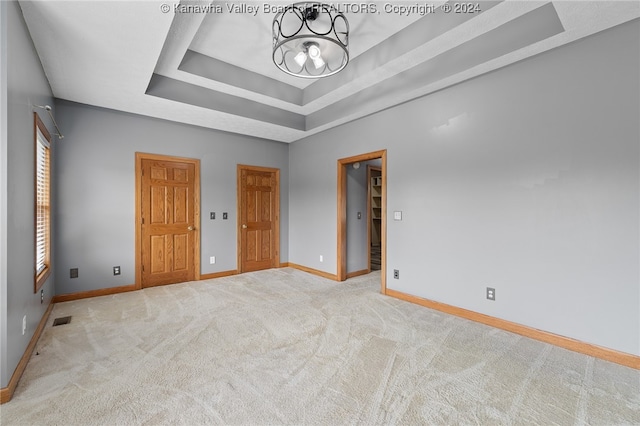 unfurnished bedroom featuring light colored carpet, a raised ceiling, and a chandelier