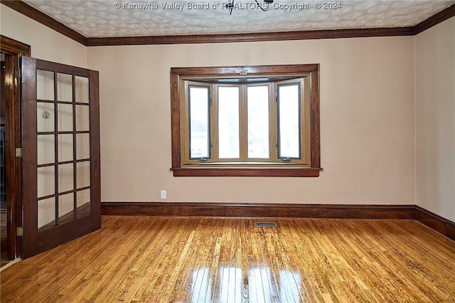 empty room with a textured ceiling, ornamental molding, and hardwood / wood-style flooring