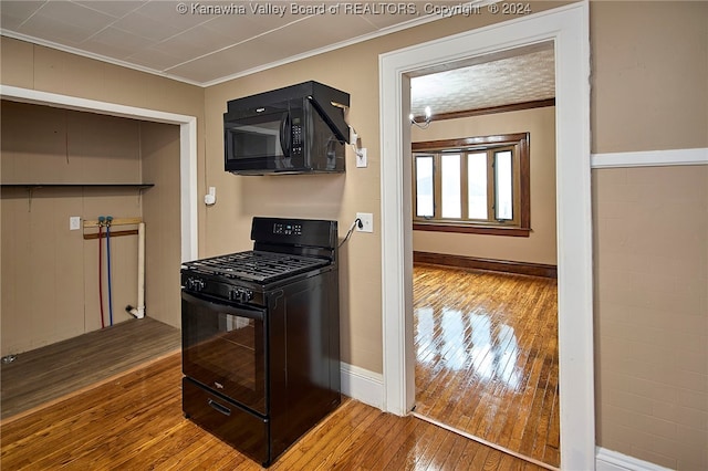 kitchen with hardwood / wood-style flooring, ornamental molding, and black appliances