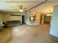 unfurnished living room with ceiling fan with notable chandelier, vaulted ceiling, and carpet