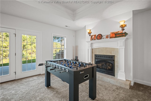 recreation room featuring a tile fireplace, a healthy amount of sunlight, crown molding, and light colored carpet