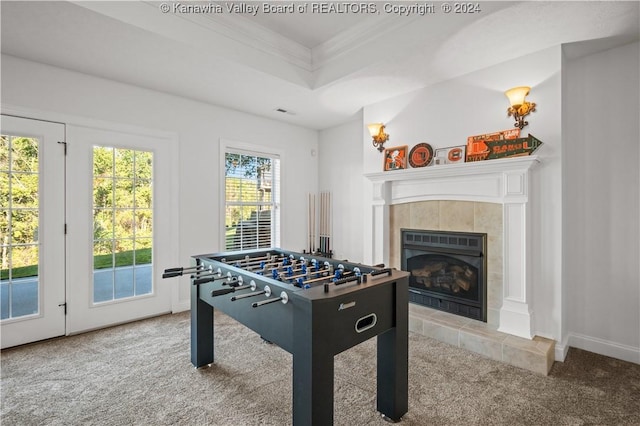 recreation room with a tiled fireplace, a tray ceiling, carpet, baseboards, and ornamental molding