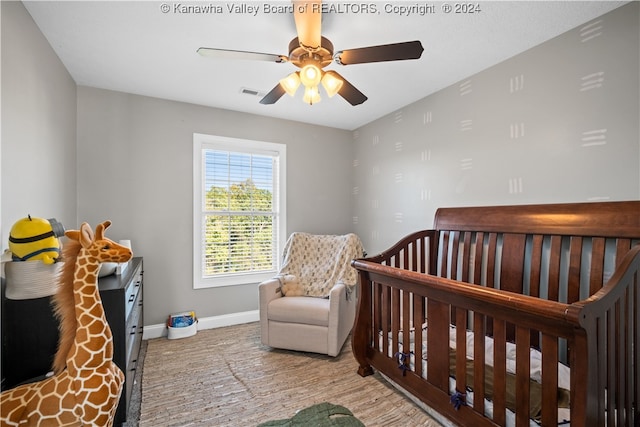 bedroom featuring light wood-type flooring, ceiling fan, and a nursery area