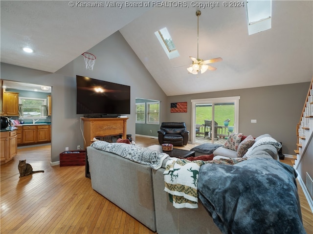 living room with ceiling fan, high vaulted ceiling, light wood-type flooring, a skylight, and sink