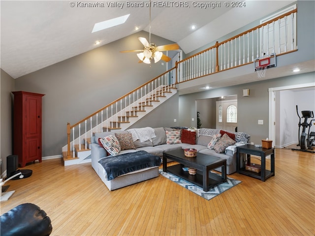 living room with ceiling fan, high vaulted ceiling, a skylight, and light wood-type flooring