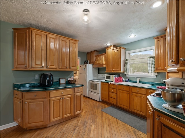 kitchen featuring white appliances, a textured ceiling, sink, and light wood-type flooring