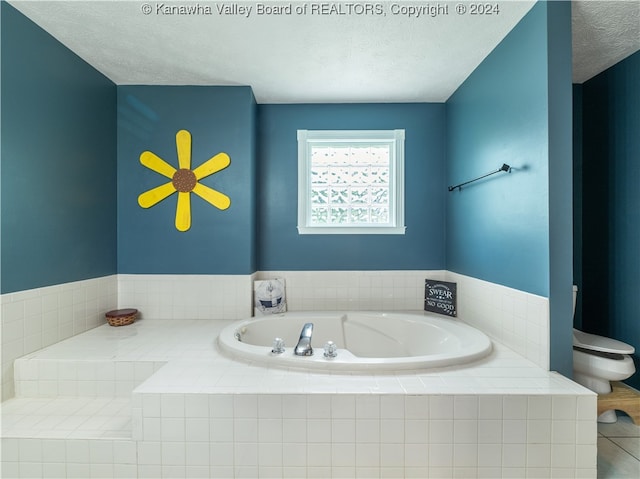 bathroom with toilet, a textured ceiling, and tiled bath