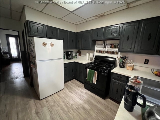 kitchen with black gas stove, light hardwood / wood-style floors, white fridge, and a paneled ceiling