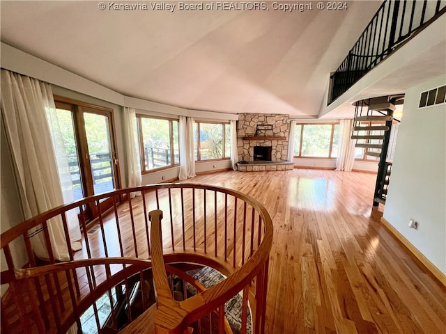 unfurnished living room with high vaulted ceiling, a wealth of natural light, hardwood / wood-style flooring, and a stone fireplace