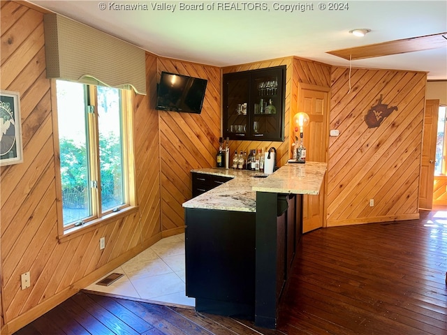 bar with light stone countertops, wood walls, dark hardwood / wood-style floors, and sink