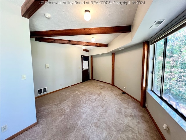 carpeted empty room with a textured ceiling, plenty of natural light, and beam ceiling