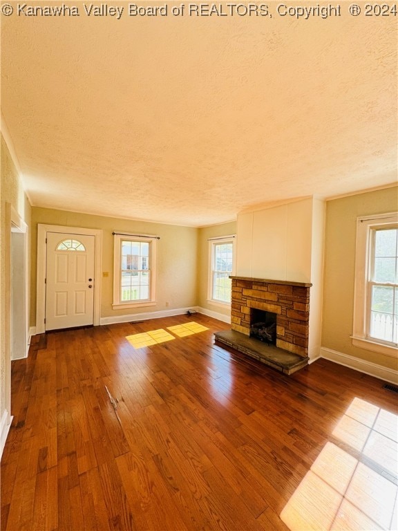 unfurnished living room featuring a stone fireplace, hardwood / wood-style floors, a healthy amount of sunlight, and a textured ceiling