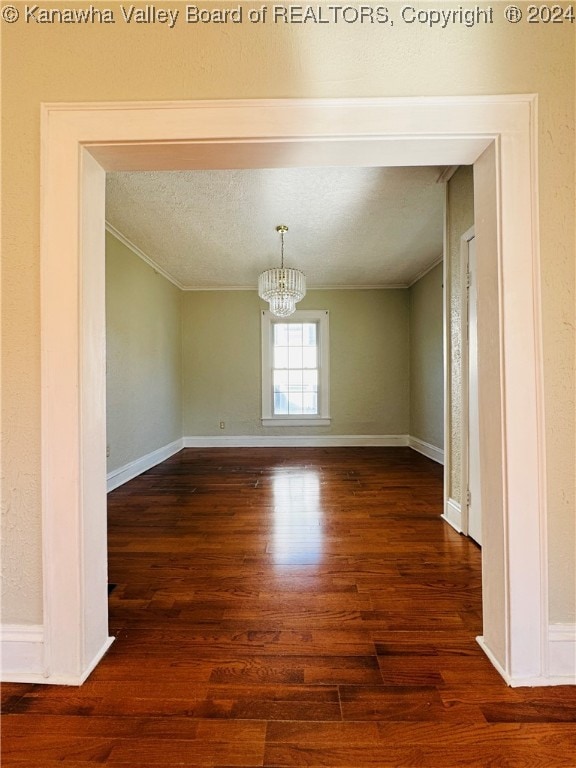 unfurnished dining area featuring crown molding, a textured ceiling, dark hardwood / wood-style floors, and an inviting chandelier