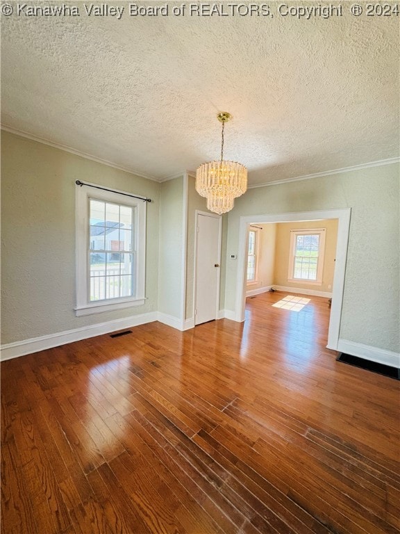 unfurnished dining area featuring ornamental molding, a textured ceiling, a notable chandelier, and hardwood / wood-style flooring