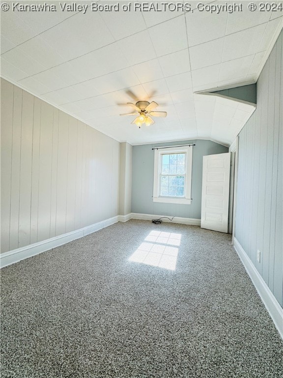 additional living space with ceiling fan, carpet, vaulted ceiling, and wooden walls