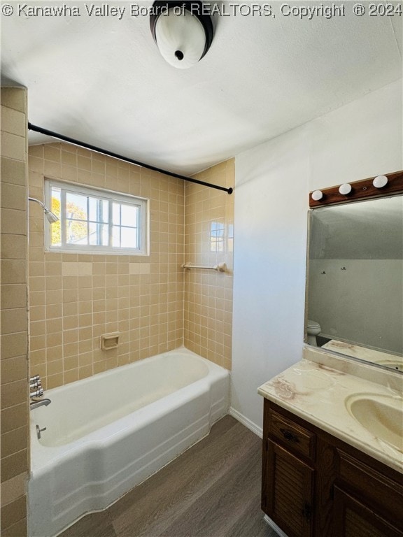 full bathroom featuring tiled shower / bath, vanity, hardwood / wood-style floors, and toilet