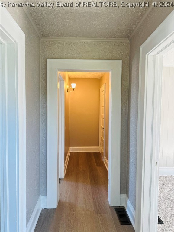 hallway with crown molding, a textured ceiling, and wood-type flooring