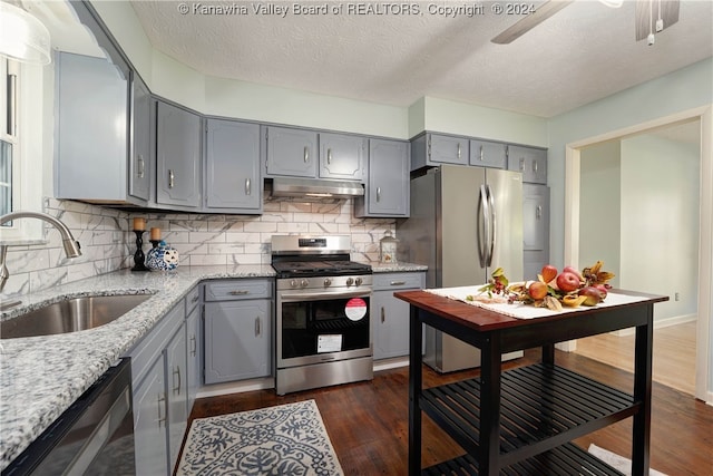 kitchen with sink, a textured ceiling, appliances with stainless steel finishes, dark hardwood / wood-style flooring, and decorative backsplash