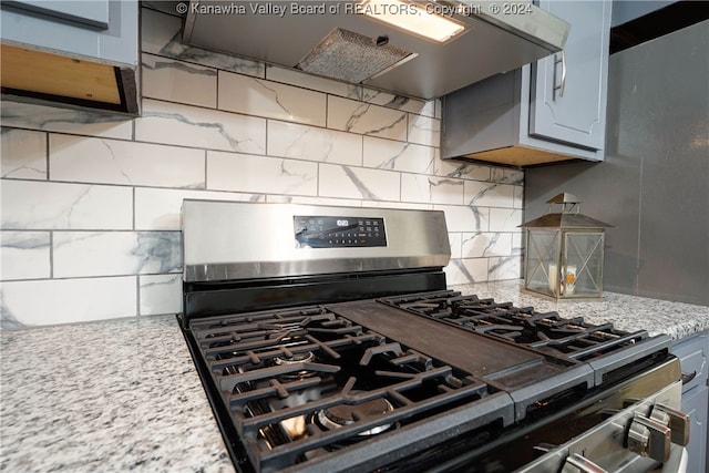 kitchen featuring wall chimney exhaust hood, gray cabinets, light stone countertops, stainless steel range with gas cooktop, and decorative backsplash