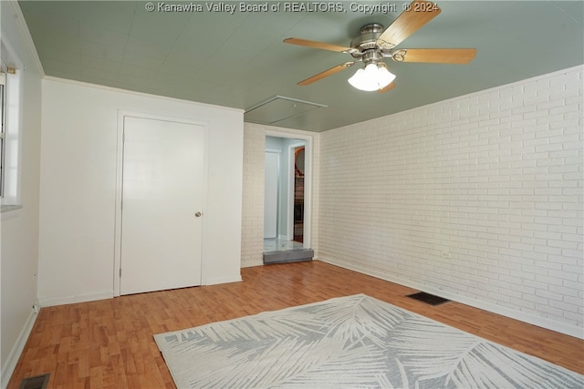 unfurnished bedroom with light hardwood / wood-style flooring, a closet, ceiling fan, and brick wall