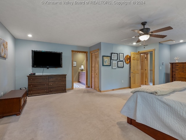 bedroom with ceiling fan, connected bathroom, a textured ceiling, and light colored carpet