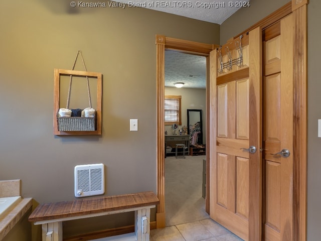 corridor with heating unit, a textured ceiling, and light colored carpet