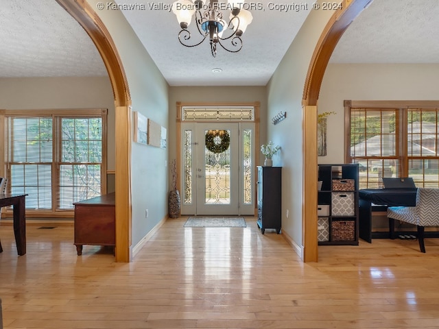 entryway with light hardwood / wood-style floors, a textured ceiling, and an inviting chandelier