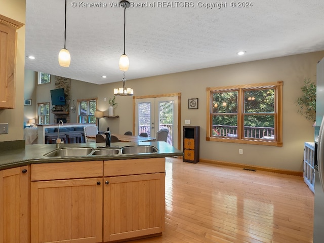 kitchen featuring a fireplace, a textured ceiling, hanging light fixtures, light hardwood / wood-style floors, and lofted ceiling