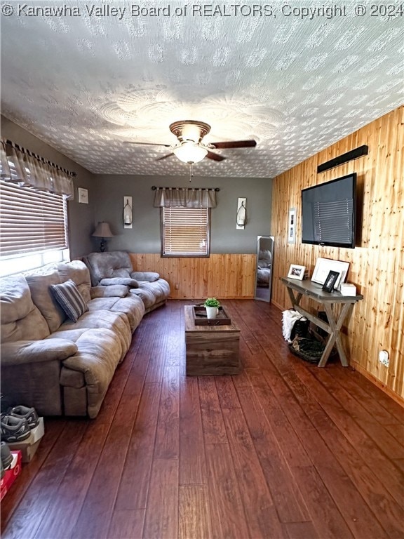 living room with ceiling fan, a textured ceiling, wood walls, and dark wood-type flooring