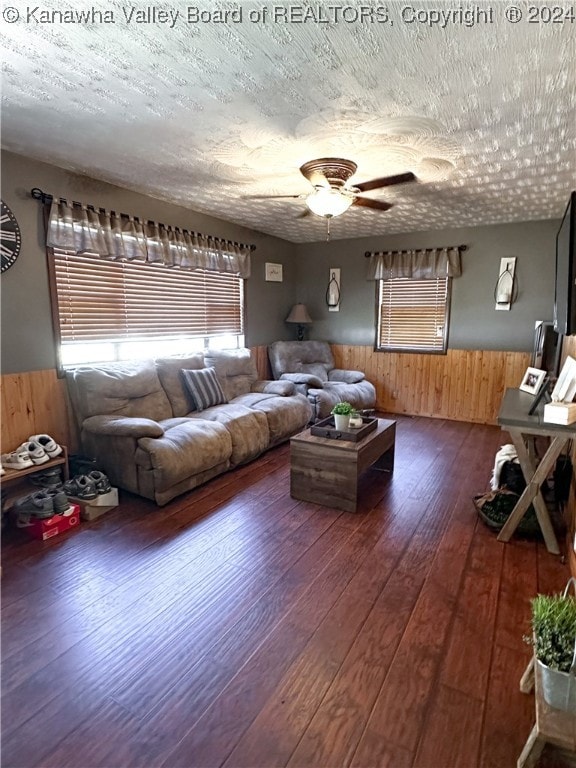 living room with ceiling fan, a textured ceiling, wood walls, and dark wood-type flooring