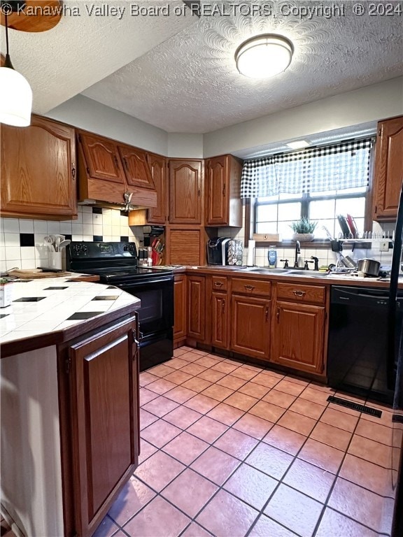 kitchen with light tile patterned flooring, tile counters, backsplash, black appliances, and a textured ceiling