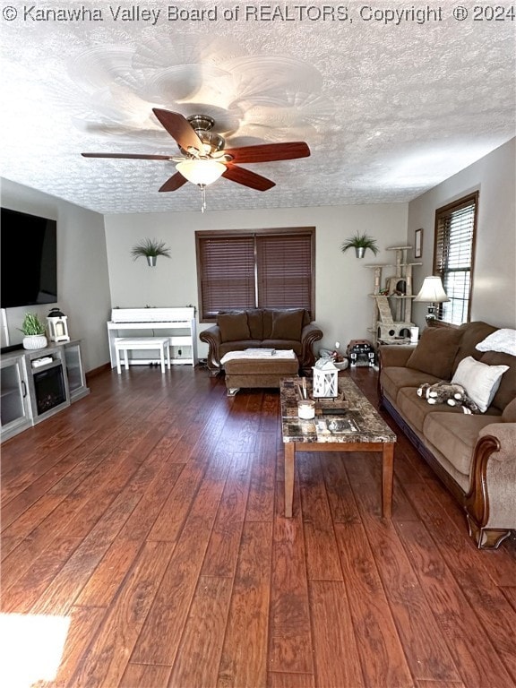 living room with dark wood-type flooring, ceiling fan, and a textured ceiling